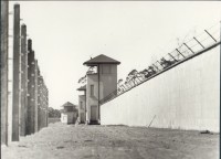 Wachturm an der Lagermauer, davor Stacheldrahtzaun (1961)